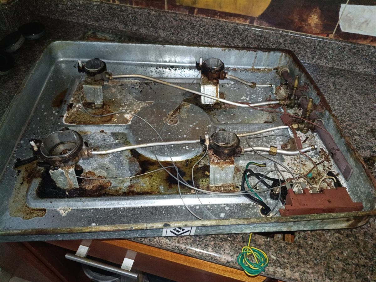 Interior de una estufa Haceb a gas antes del mantenimiento: bandeja con grasa acumulada, válvulas y empaques vencidos