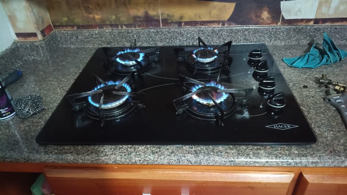 Estufa Haceb de vidrio negro con los cuatro quemadores encendidos en llama azul después del mantenimiento